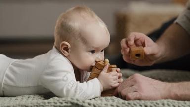 白种人家庭难以辨认的父亲爸爸和小女儿儿子新生儿幼儿躺在地板上玩玩具宝宝咬木结构的概念，男人抚摸着脑袋